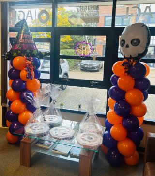 two orange and purple halloween balloon towers. table in the middle of the balloon towers with five sweet platters